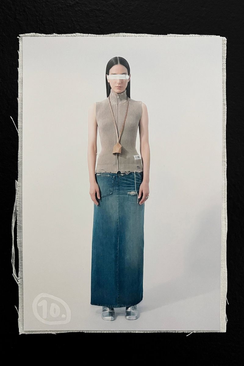 Fashion shot featuring a woman in a tan top and long blue denim skirt, standing in front of a white background, captured in studio lighting.