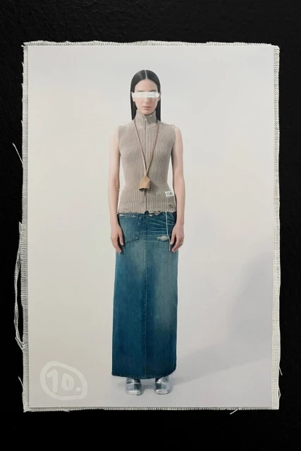 Fashion shot featuring a woman in a tan top and long blue denim skirt, standing in front of a white background, captured in studio lighting.