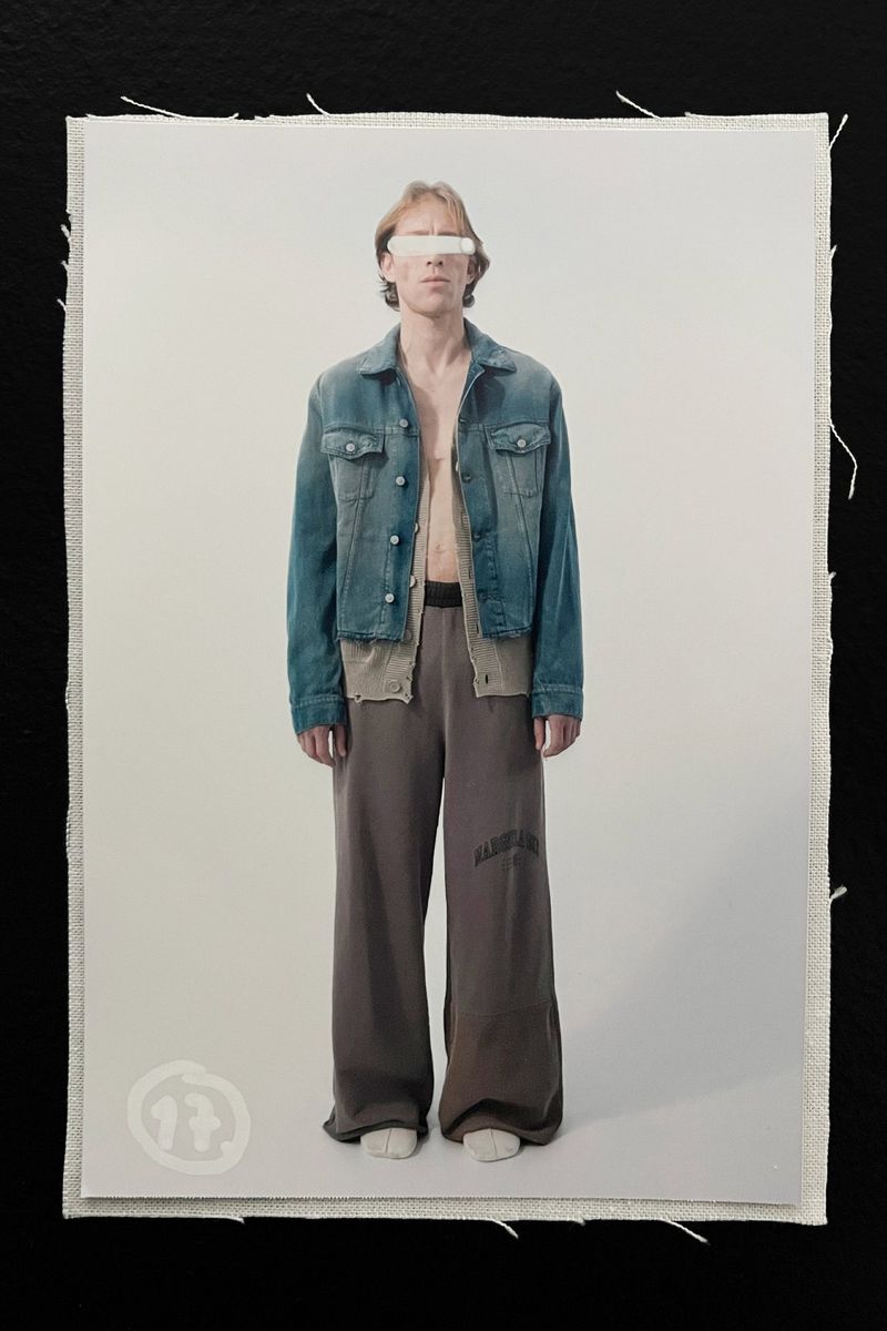 Full shot of a male model in casual streetwear, standing on a white backdrop, wearing a denim jacket and loose-fitting brown pants.