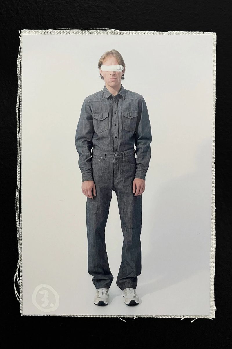 Full-length studio shot of an adult male fashion model posing in a denim shirt and jeans with running shoes on a white backdrop.