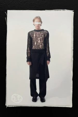 Fashion photo of a slender adult wearing a black knit sweater and long skirt-like wrap against a white backdrop on black material.