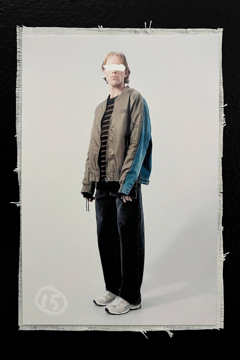 Full-length studio shot of a young adult in stylish streetwear, including a bomber jacket, wide-leg jeans, and chunky sneakers, against a neutral background.
