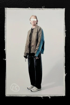 Full-length studio shot of a young adult in stylish streetwear, including a bomber jacket, wide-leg jeans, and chunky sneakers, against a neutral background.