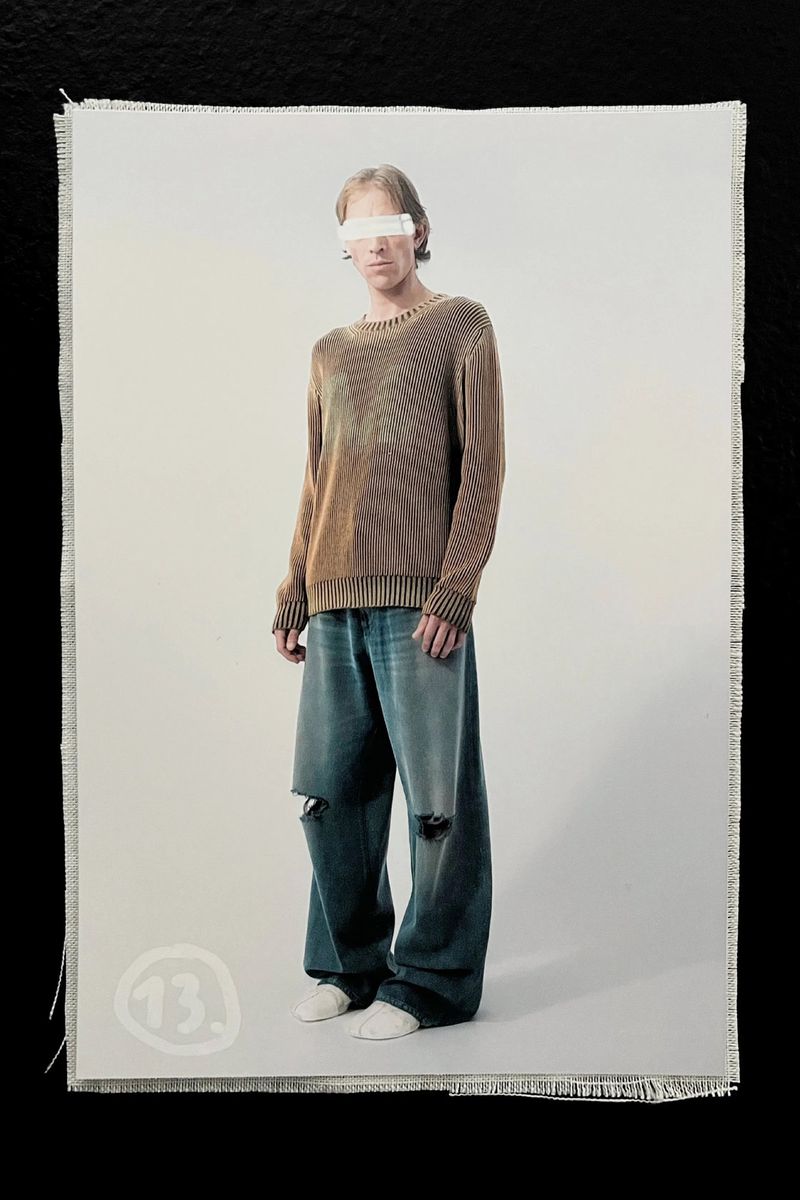 Full shot of a person wearing a brown sweater and wide-leg, ripped jeans in front of a white backdrop on a canvas-like material.