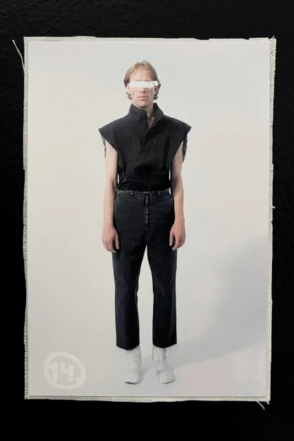 Model wearing a black sleeveless top and dark trousers with white split-toe boots against a white studio background.