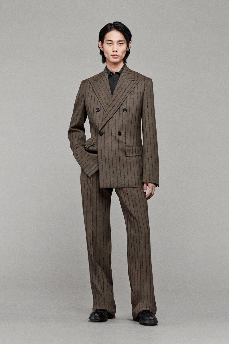 An Asian man wearing a patterned double-breasted suit is posing indoors. He has a neutral expression and is looking at the camera.