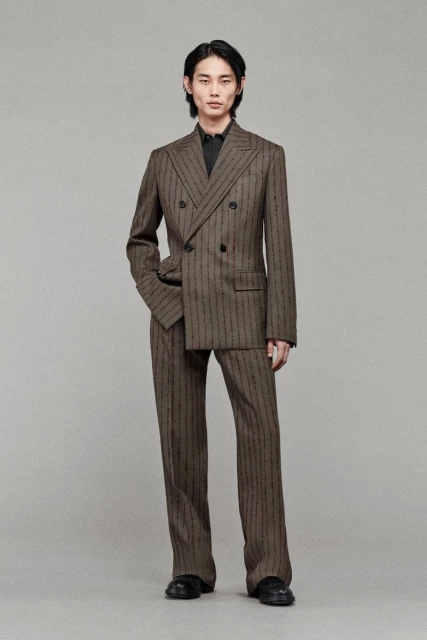 An Asian man wearing a patterned double-breasted suit is posing indoors. He has a neutral expression and is looking at the camera.