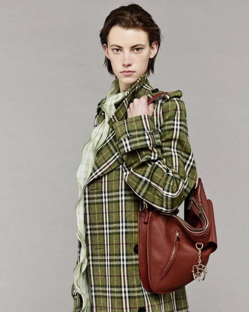 Fashion image of a stylish adult woman wearing a green plaid coat and holding a brown leather shoulder bag in a studio setting.