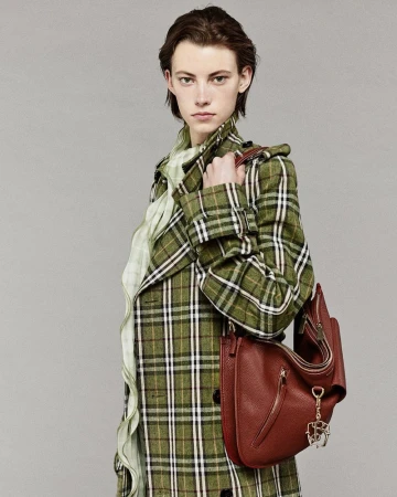 Fashion image of a stylish adult woman wearing a green plaid coat and holding a brown leather shoulder bag in a studio setting.