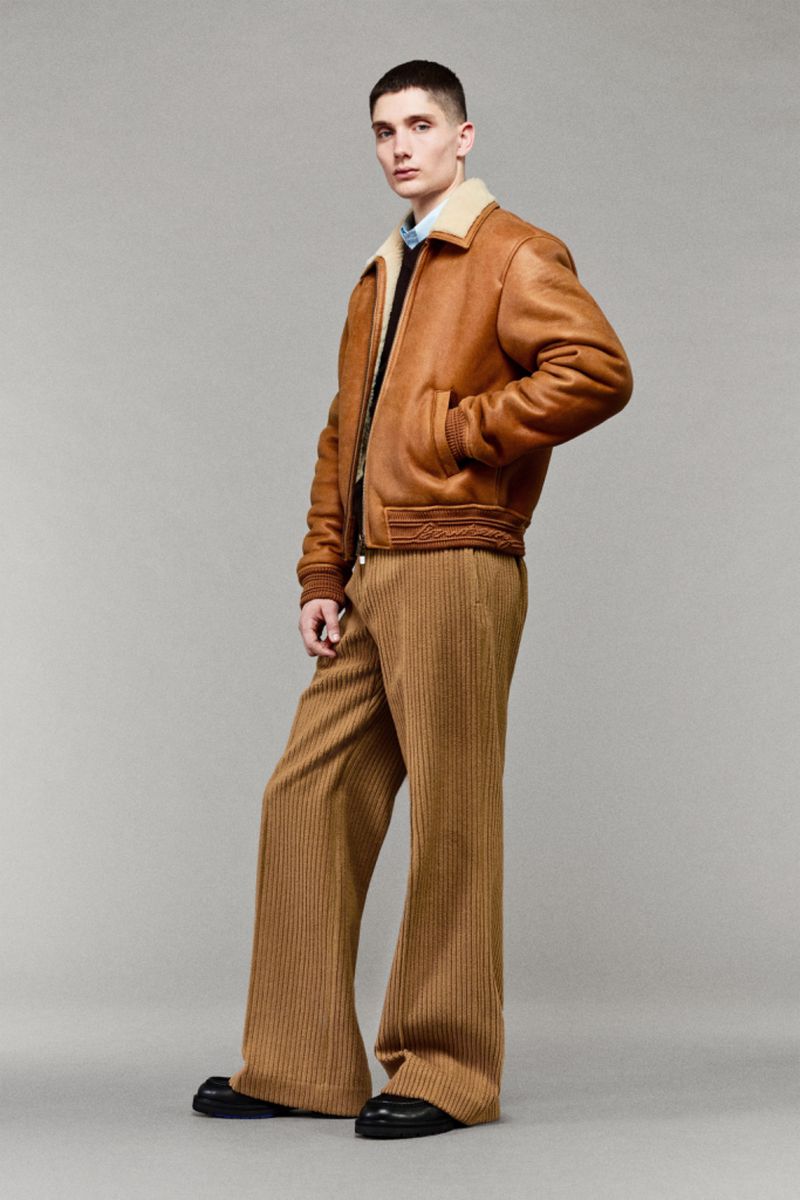 Full-body shot of a slender male model in a light brown jacket with a beige collar and wide corduroy pants, posing in a photo studio.
