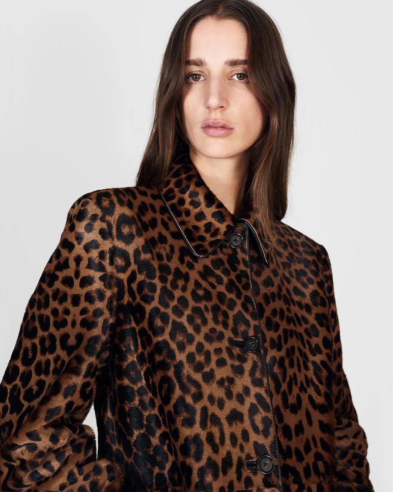Portrait of a woman wearing a brown and black spotted coat, posing in front of a neutral background in a fashion studio setting.