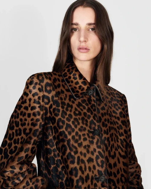 Portrait of a woman wearing a brown and black spotted coat, posing in front of a neutral background in a fashion studio setting.