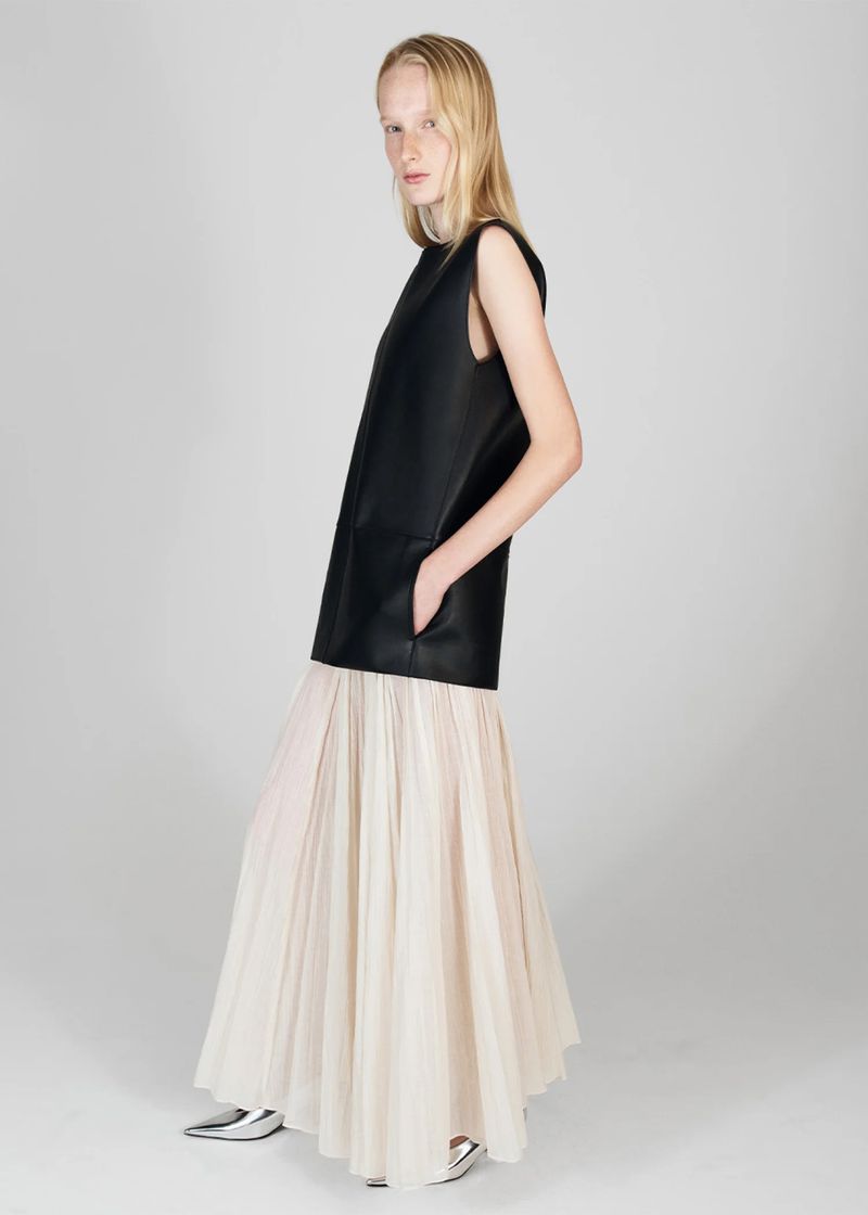 Fashion shoot: a slender woman with blonde hair poses in a sleeveless black top and a long, flowing, light-beige skirt in a studio.