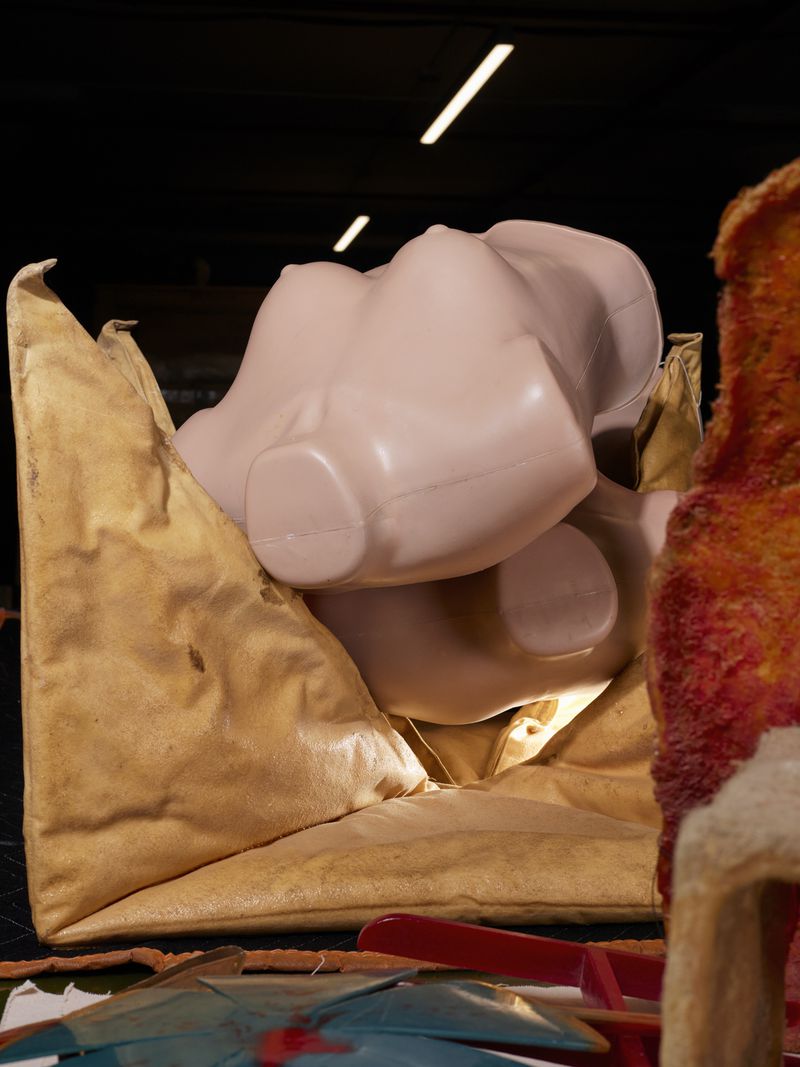 Still life of a crumpled brown bag containing several pale pink plastic mannequin torsos, with an out-of-focus partial animal figurine.
