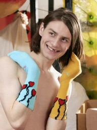 Young man smiling with brown hair holding blue and yellow socks over his shoulders for SSENSE Gaetano Pesce project