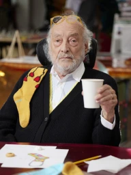 Elderly man with white beard wearing yellow glasses and black cardigan holding white cup for SSENSE Gaetano Pesce project