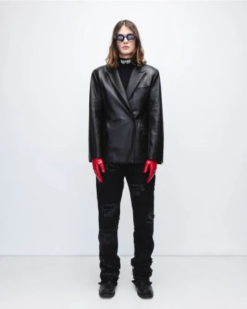 Adult male fashion model in a black leather jacket, black ripped jeans, red gloves, and sunglasses poses in a photo studio.