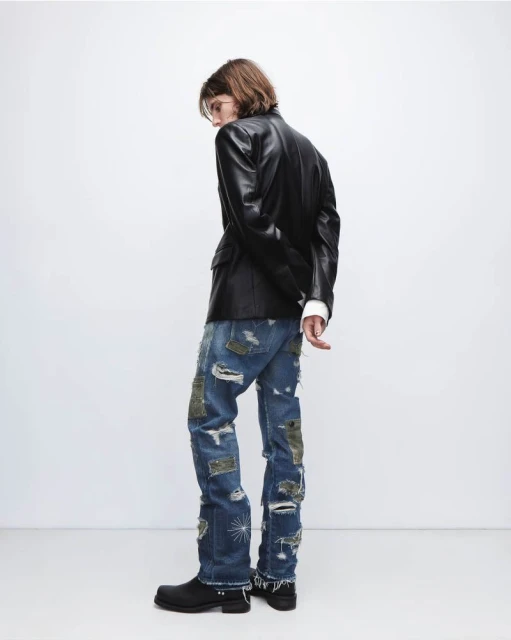 Fashionable adult male wearing a black leather jacket and distressed denim pants, posing in a white studio, showcasing street style.