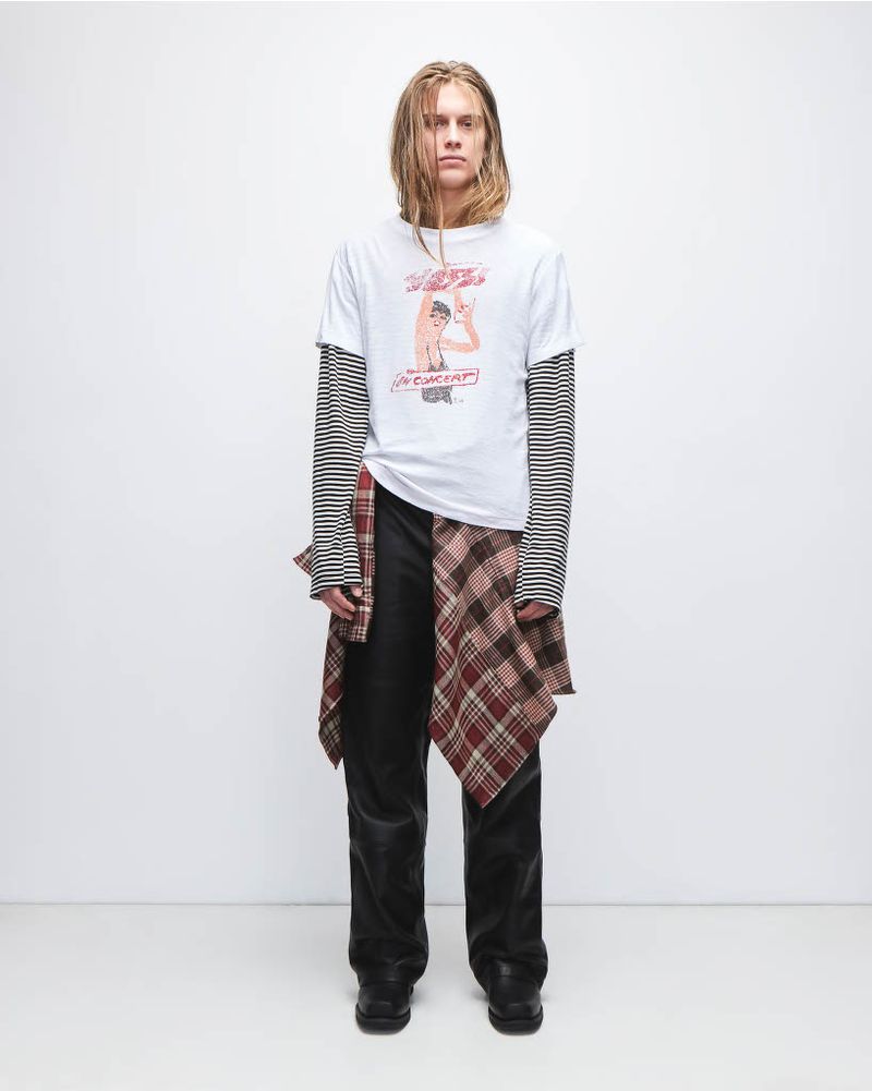 Full-length portrait of a slender adult man wearing a graphic tee, long-sleeve top, dark denim jeans, and shoes in a photo studio.