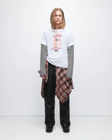 Full-length portrait of a slender adult man wearing a graphic tee, long-sleeve top, dark denim jeans, and shoes in a photo studio.