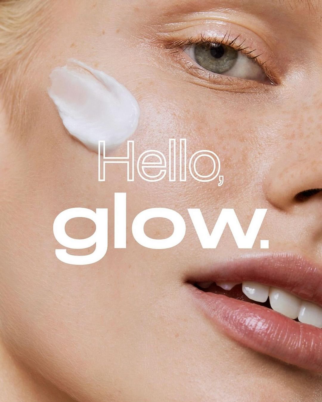 Close-up of a fair-skinned adult female face with cream applied on her cheek; copy reads 'Hello, glow.' Beauty, skin, face treatment concept.