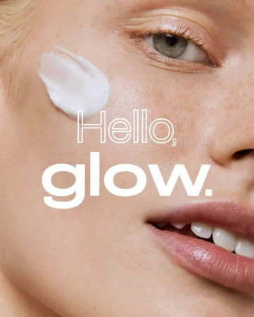Close-up of a fair-skinned adult female face with cream applied on her cheek; copy reads 'Hello, glow.' Beauty, skin, face treatment concept.