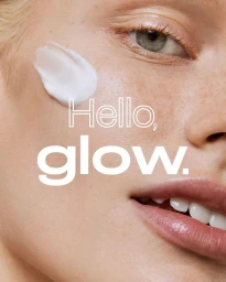 Close-up portrait of a woman's face with a dab of white skincare cream on her cheek and bold typography reading Hello glow.