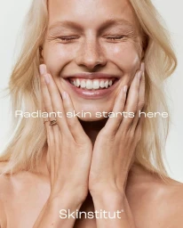 Close-up portrait of a smiling blonde woman with her hands pressed against her cheeks against a white background