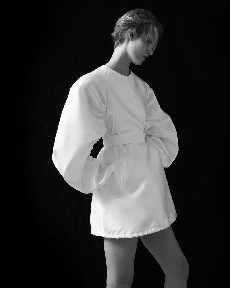 Model in a white belted dress with voluminous puff sleeves against a dark background for Bon Bride lookbook