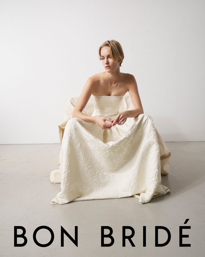 Woman in strapless dress sitting in studio. Light-skinned female model with short blonde hair poses for a fashion shot in white gown.