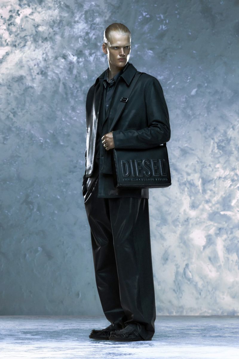 Man in black fashion, wearing a Diesel bag in a studio with marble effect backdrop, stylish and modern, full length shot.