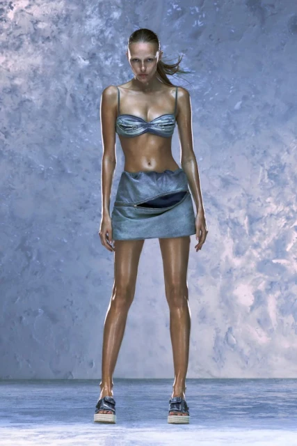 A full portrait of a young adult female fashion model wearing a blue two-piece outfit with platform sandals in a photo studio setting.