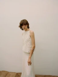 Model with short brown hair wearing a white crochet top against a pale neutral background