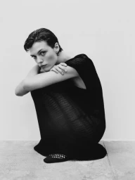 Model wearing a black crochet dress crouching against a plain background