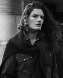 Monochrome portrait of a woman with long curly hair wearing a denim shirt and sweater draped over her shoulders