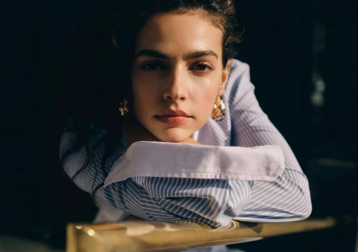 Portrait of a woman wearing a blue striped shirt leaning on her arms against a dark background