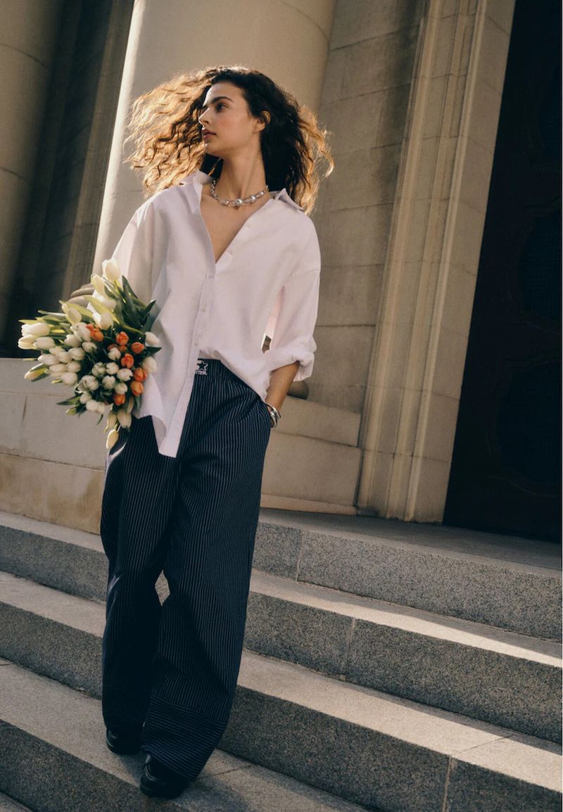 Woman in white shirt and pinstripe trousers walking down stone steps holding flowers