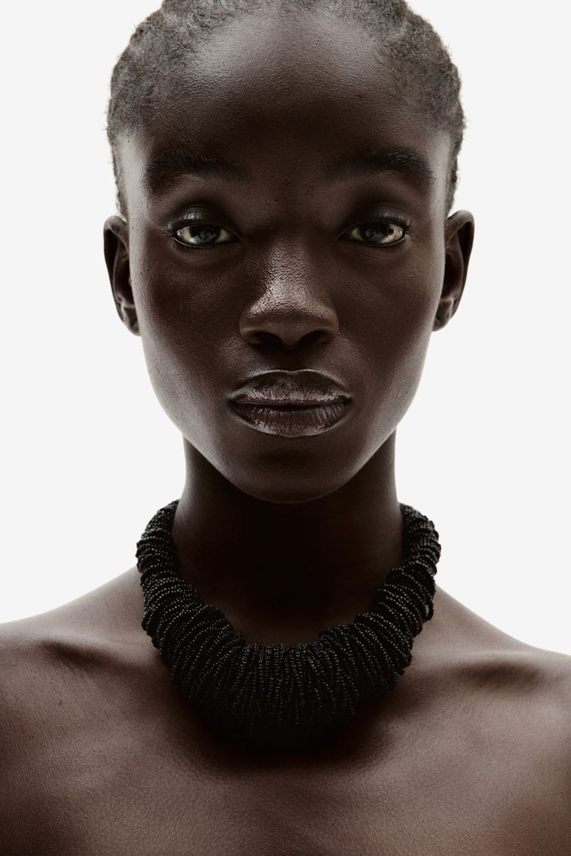 Close-up studio shot of an African-descent adult female model wearing a black beaded necklace against a white background.
