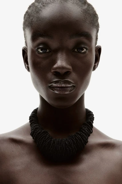 Close-up studio shot of an African-descent adult female model wearing a black beaded necklace against a white background.