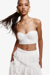 Model wearing a white strapless crop top and tiered skirt against a bright white background.