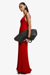 Model in long red dress holding a large black mesh handbag against a white background