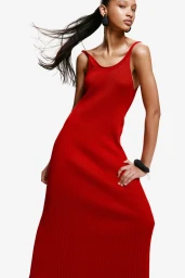 Model wearing a long red ribbed dress with dark accessories against a white background