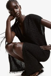 Model in a black knit dress crouching against a white background for H&M summer 2024 lookbook