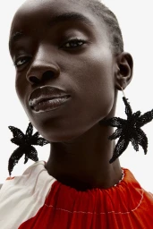Close-up portrait of a Black female model wearing large beaded star-shaped earrings and a red and white top
