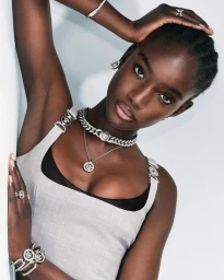 Model wearing silver jewellery and a grey dress against a white background for Versace Summer 2024 by Ilya Lipkin.