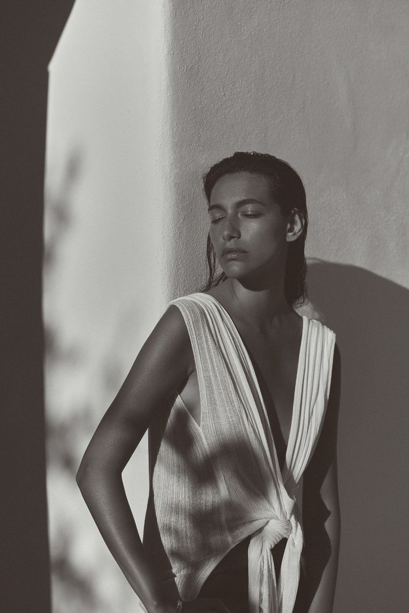 Monochrome portrait of an adult woman with eyes closed wearing a sleeveless top, partially lit by sunlight and shadowed by trees.