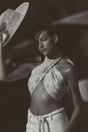Model Nour Rizk wearing a floral halter top and white trousers holding a woven hat for Anthropologie Linen project