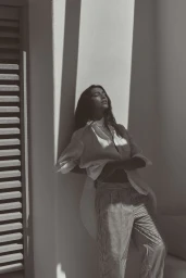 Model Nour Rizk leaning against a wall in a white shirt and striped trousers for Anthropologie Linen