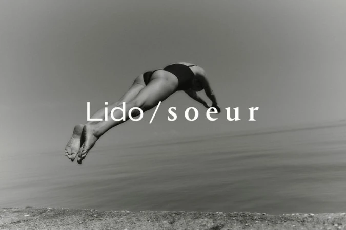 Monochrome image of a woman in a swimsuit diving into the ocean, captured with a low angle against a clear sky and horizon line.