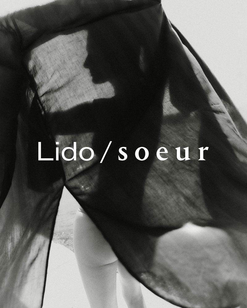 Monochrome studio shot of a draped female figure with visible text overlayed. The fabric creates a dark silhouette and implied nudity.
